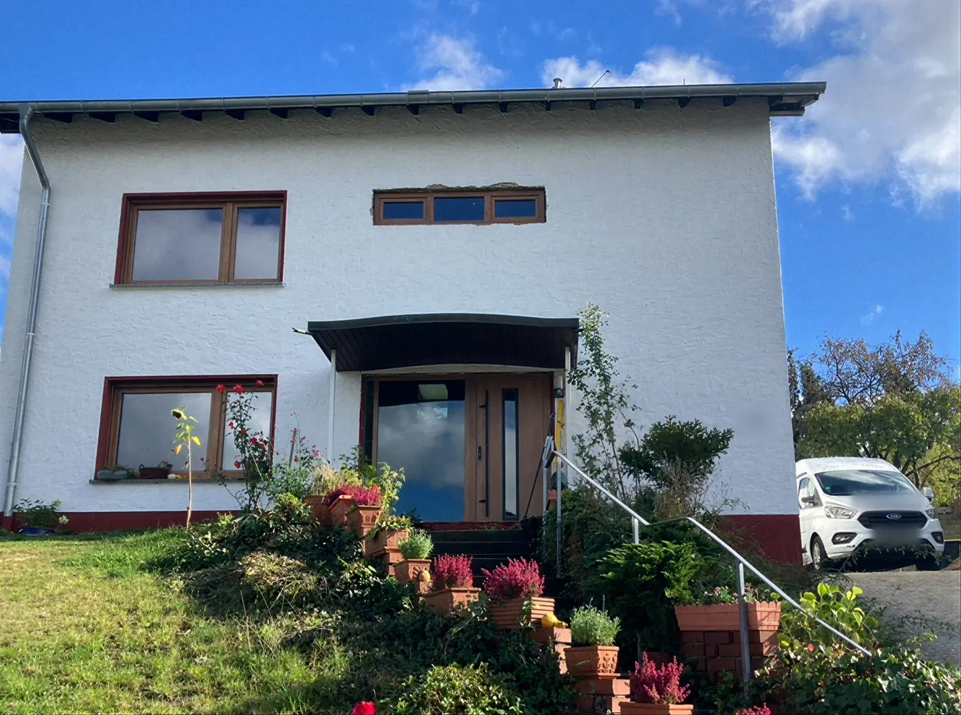 Weißes Haus am Hang mit neuen Fenstern in Holzoptik und einer Eingangstür mit seitlichem Glas unter einem Vordach