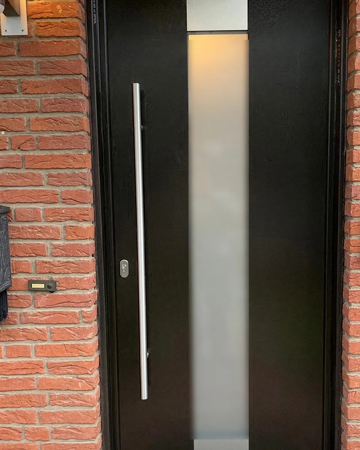Schwarze Haustür mit mattem Glasstreifen und Edelstahl-Stangengriff in rotem Klinker